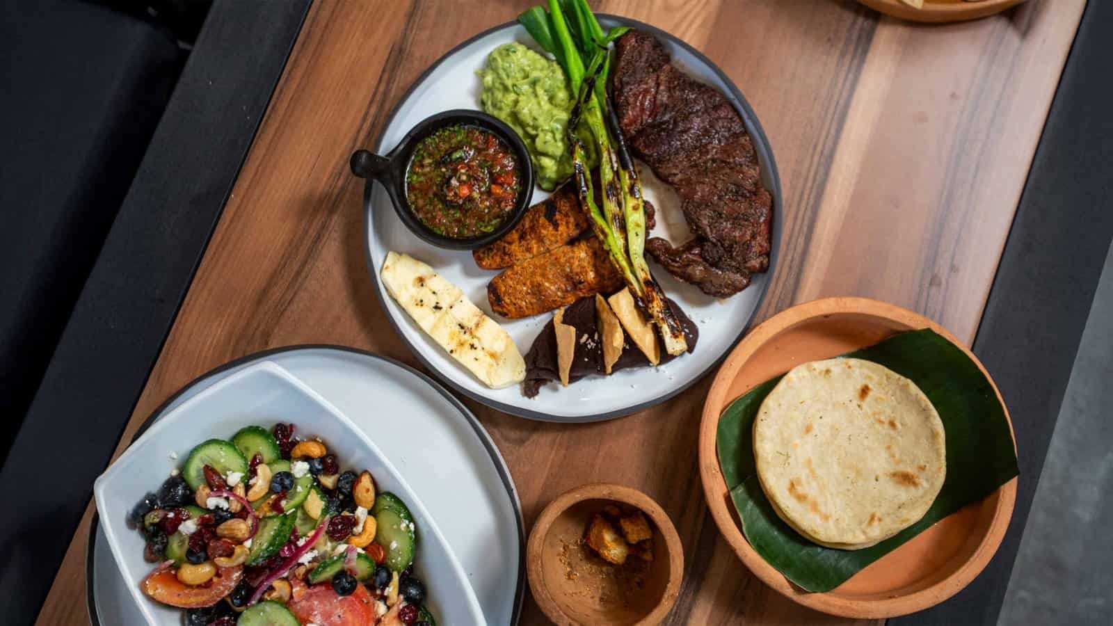 Signature Churrasco Ancestral steak dinner with chimichurri, grilled vegetables, Greek Salad, and fresh tortillas served in traditional clay bowls at Balam Bistro Copán